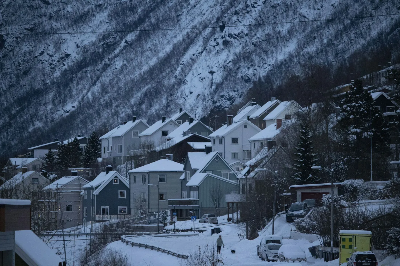 Wooden houses on a snowy hillside street in Narvik below a steep, snow-streaked mountain face
